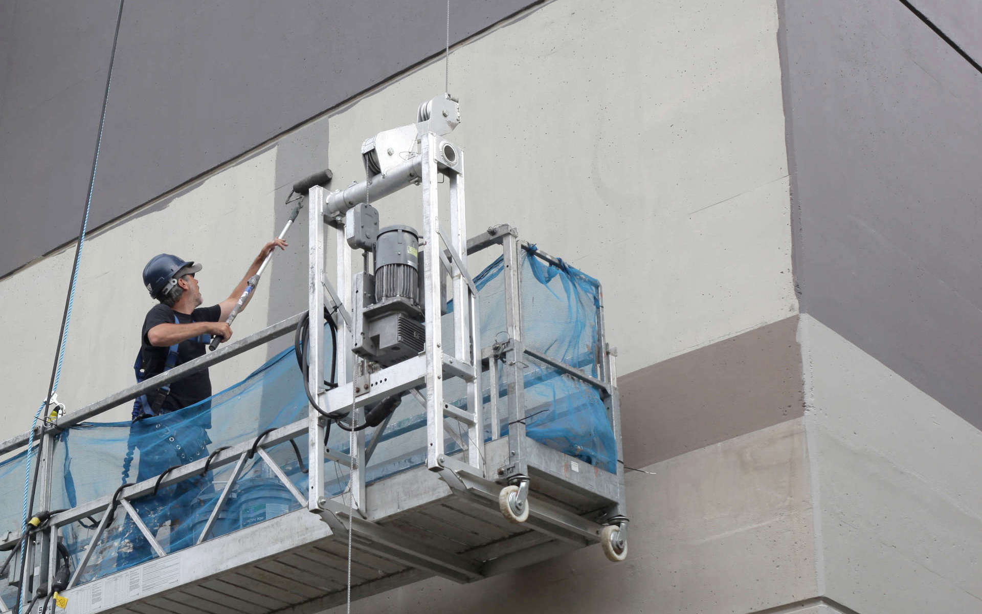 High rise building exterior painter, painting with a roller on a weigh stage rig. A commercial and multi-unit residential high-rise exterior renovation, refresh, update - painting, caulking and coating. A high-rise painting project by Performance Painting and Caulking Ltd.